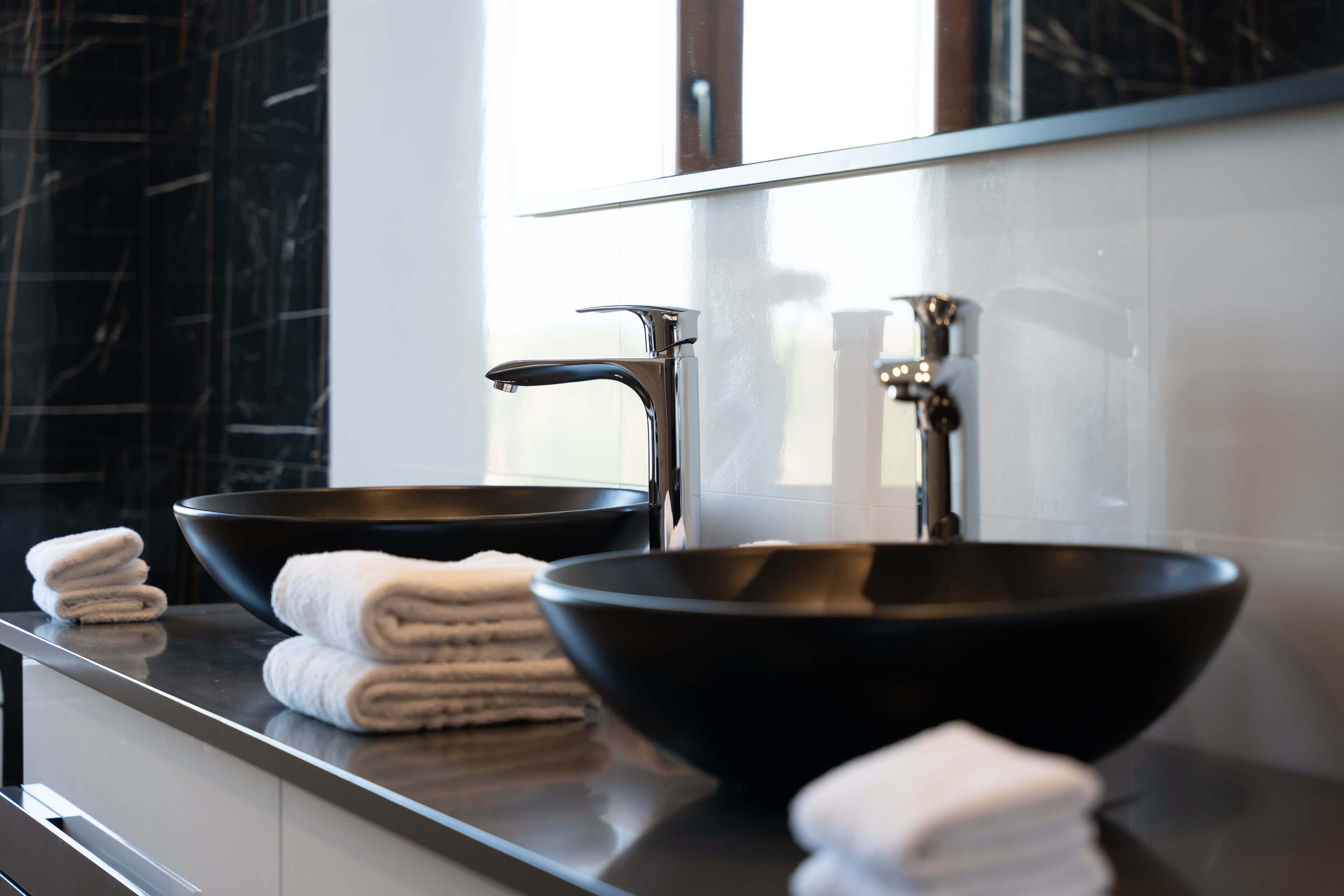 A modern bathroom with two black bowls as sinks, a large mirror, and neatly folded towels on the counter.
