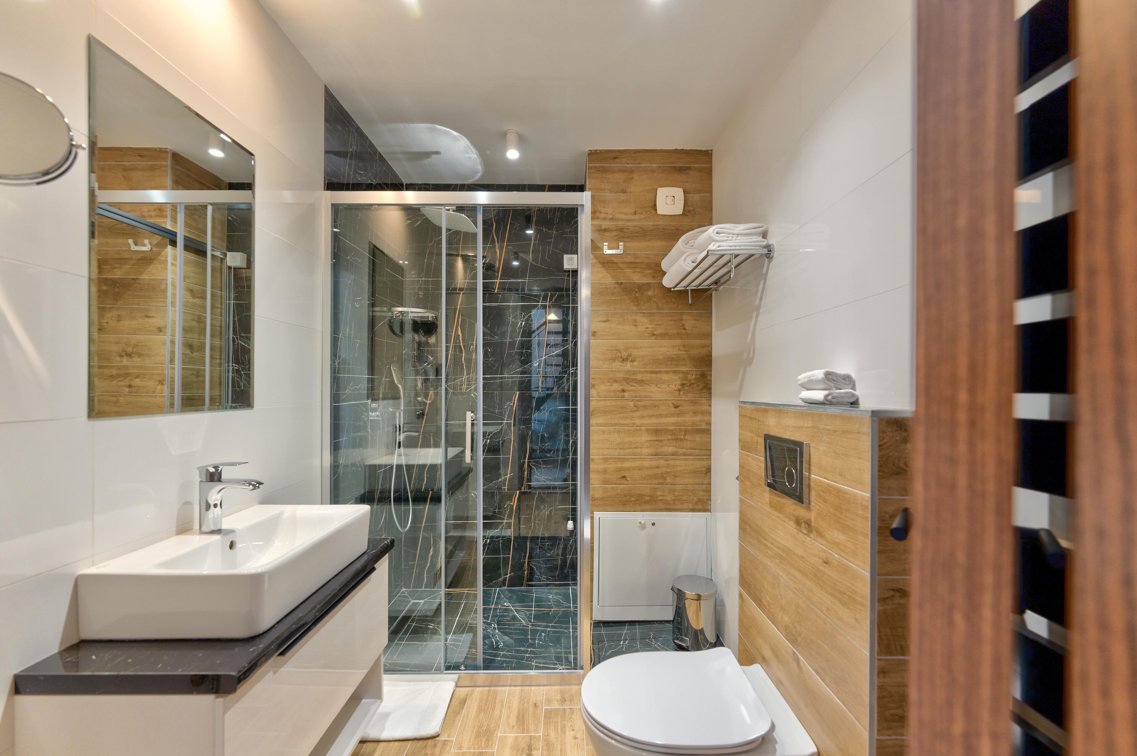 Un baño moderno con cabina de ducha de vidrio, un lavabo blanco y un mueble de tocador de madera.