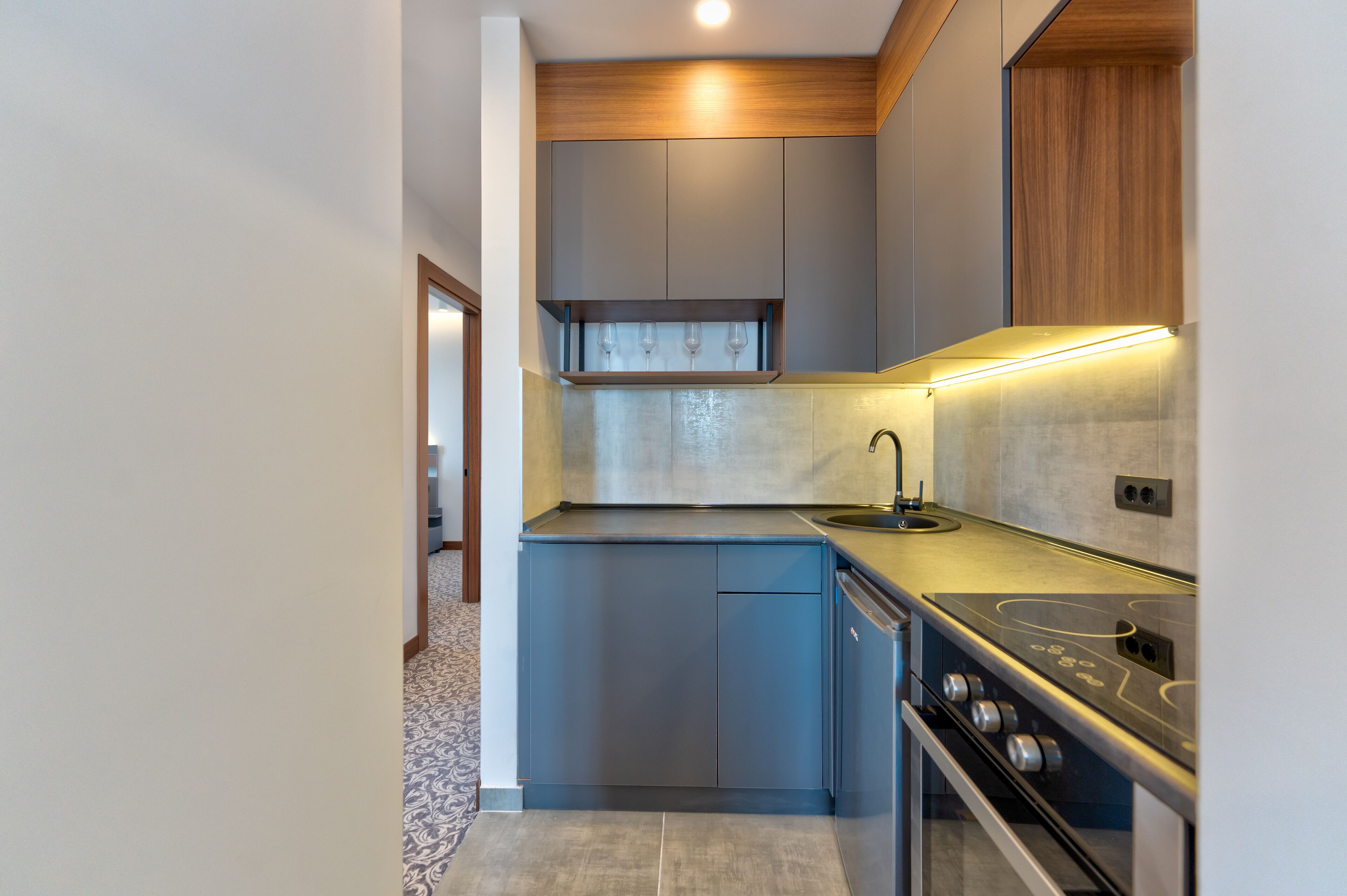 A compact kitchen with grey cabinets, a stainless steel stove, and a wooden upper shelf.
