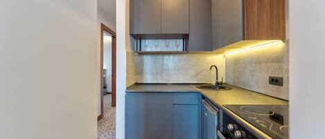 A compact kitchen with grey cabinets, a stainless steel stove, and a wooden upper shelf.