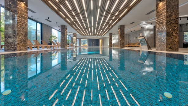 Una piscina interior moderna con carriles bien definidos, columnas de mármol e iluminación lineal en el techo.