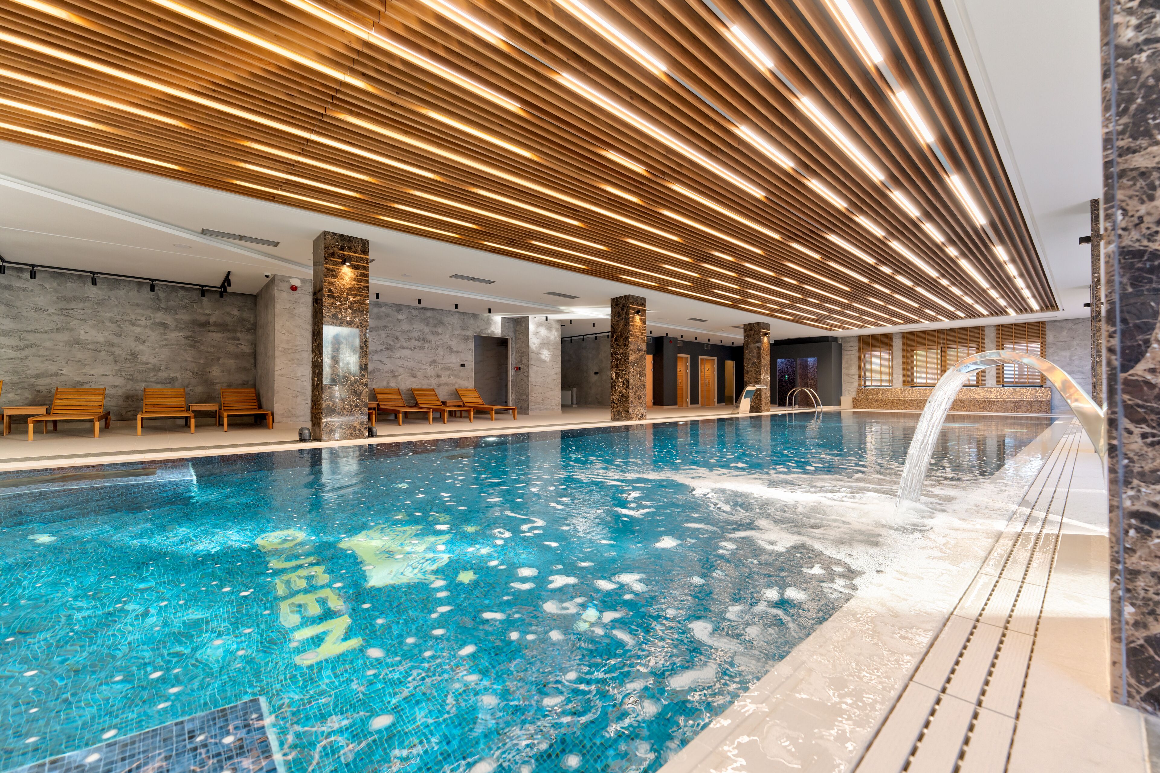 Piscina interior moderna con techo de madera y una fuente.