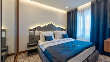 A modern hotel room with a large bed, a headboard with a mountain design, a bedside table, and a window with curtains.