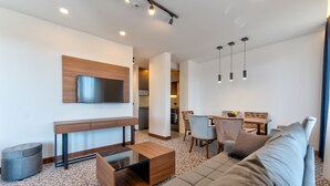 Una sala de estar moderna con un sofá, una mesa de centro y un televisor montado en la pared. Hay una zona de comedor con sillas y una mesa.