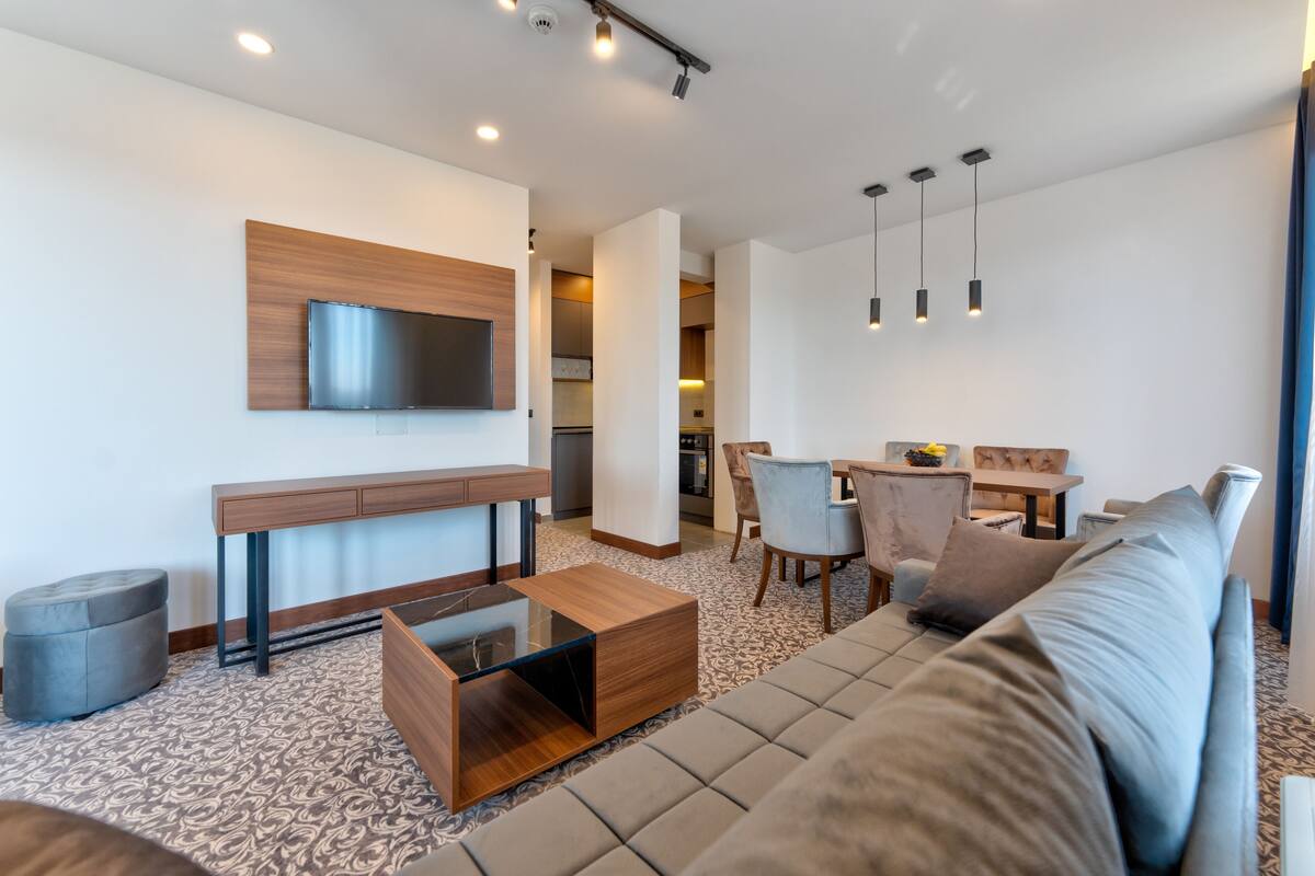 Un salon moderne avec un canapé, une table basse et un téléviseur fixé au mur. On y trouve également un coin repas avec des chaises et une table.