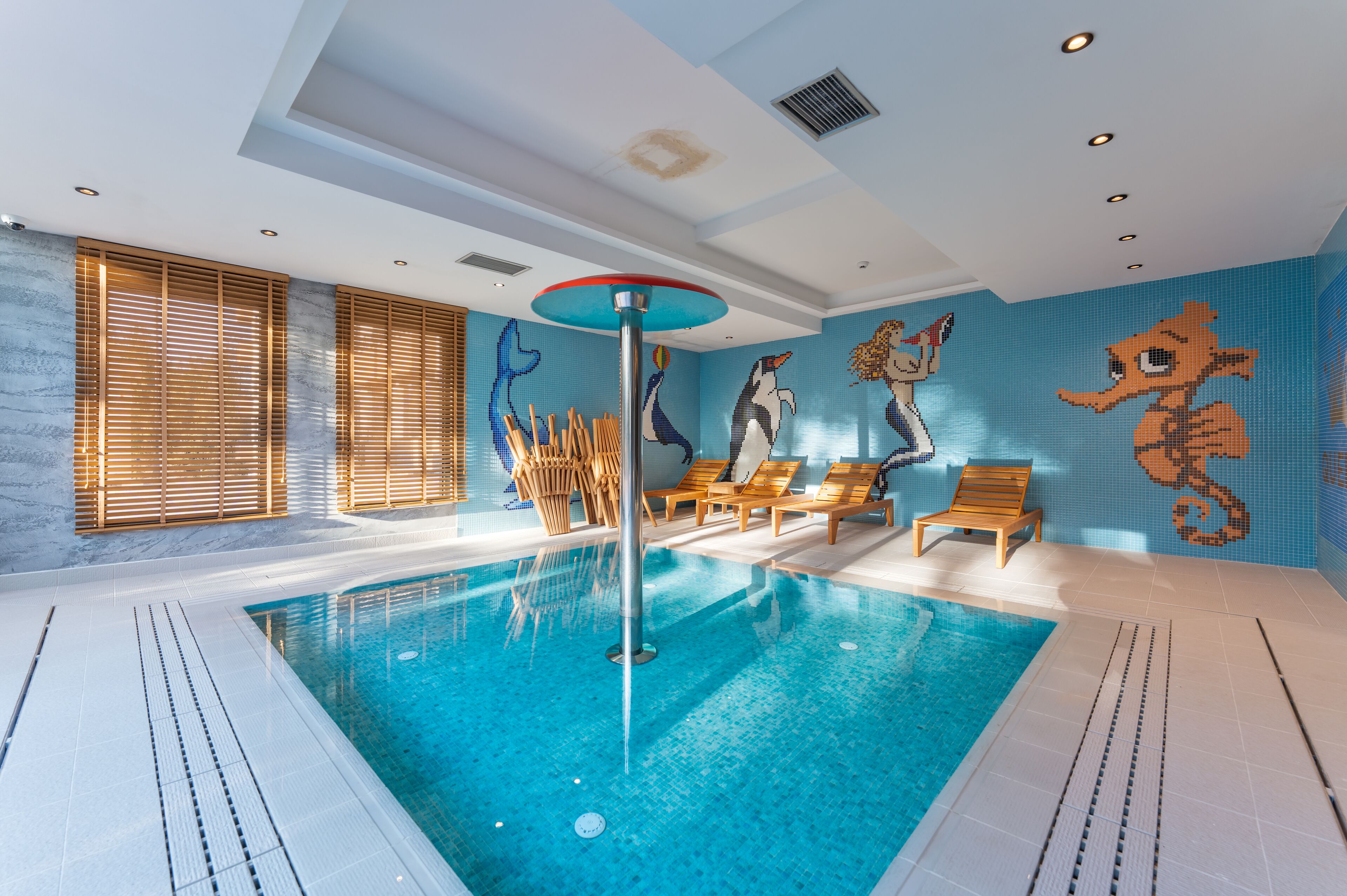 An indoor swimming pool with wooden loungers and a mural of sea creatures.