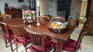 Un coin repas avec une table en bois, des chaises, un vase de fleurs et un panier de fruits.