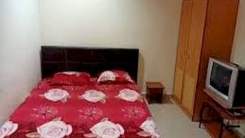 A bedroom with a bed, a television on a stand, and a wardrobe.