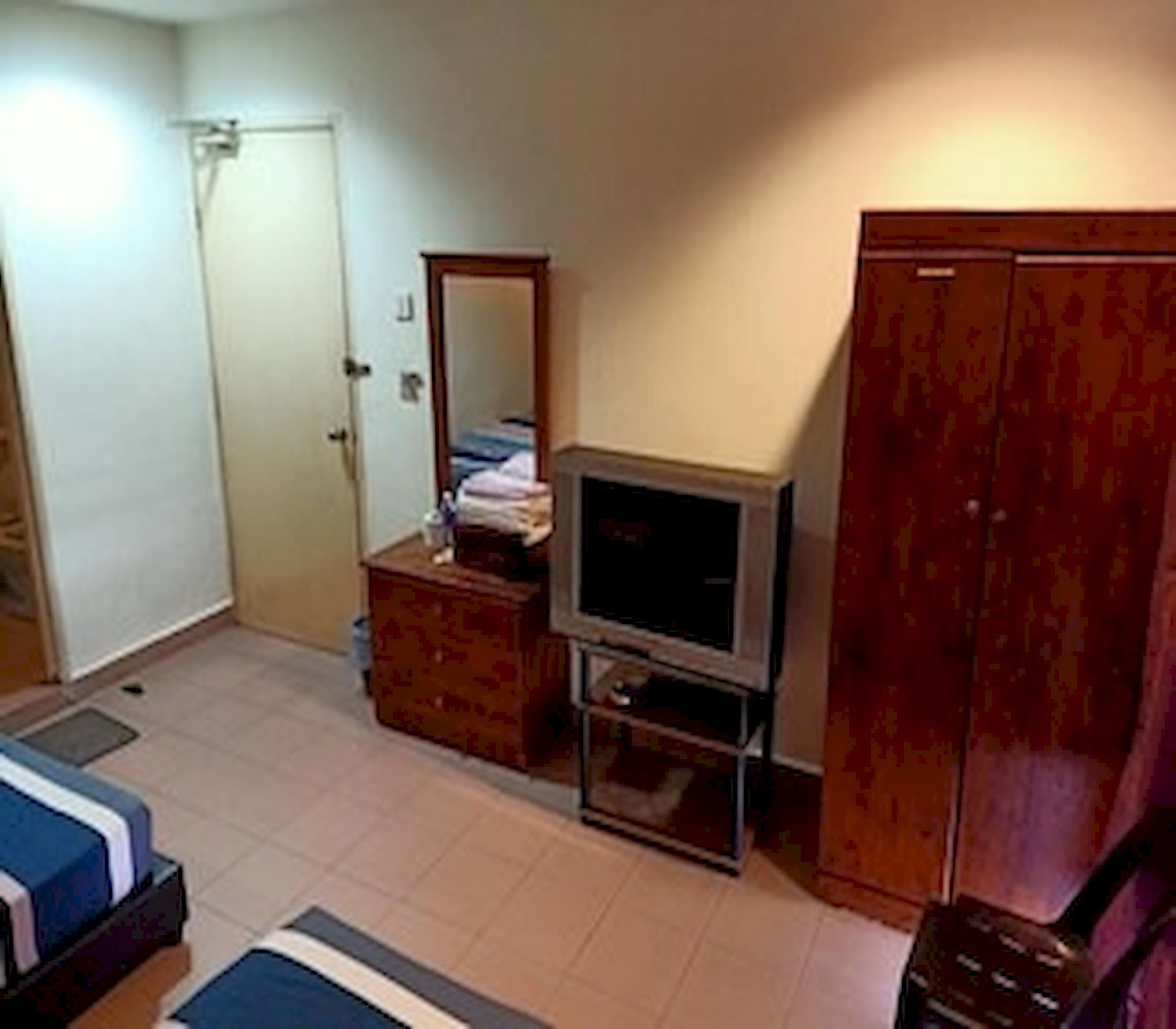 Una habitación con una cama, un televisor sobre un mueble, un armario y una puerta.