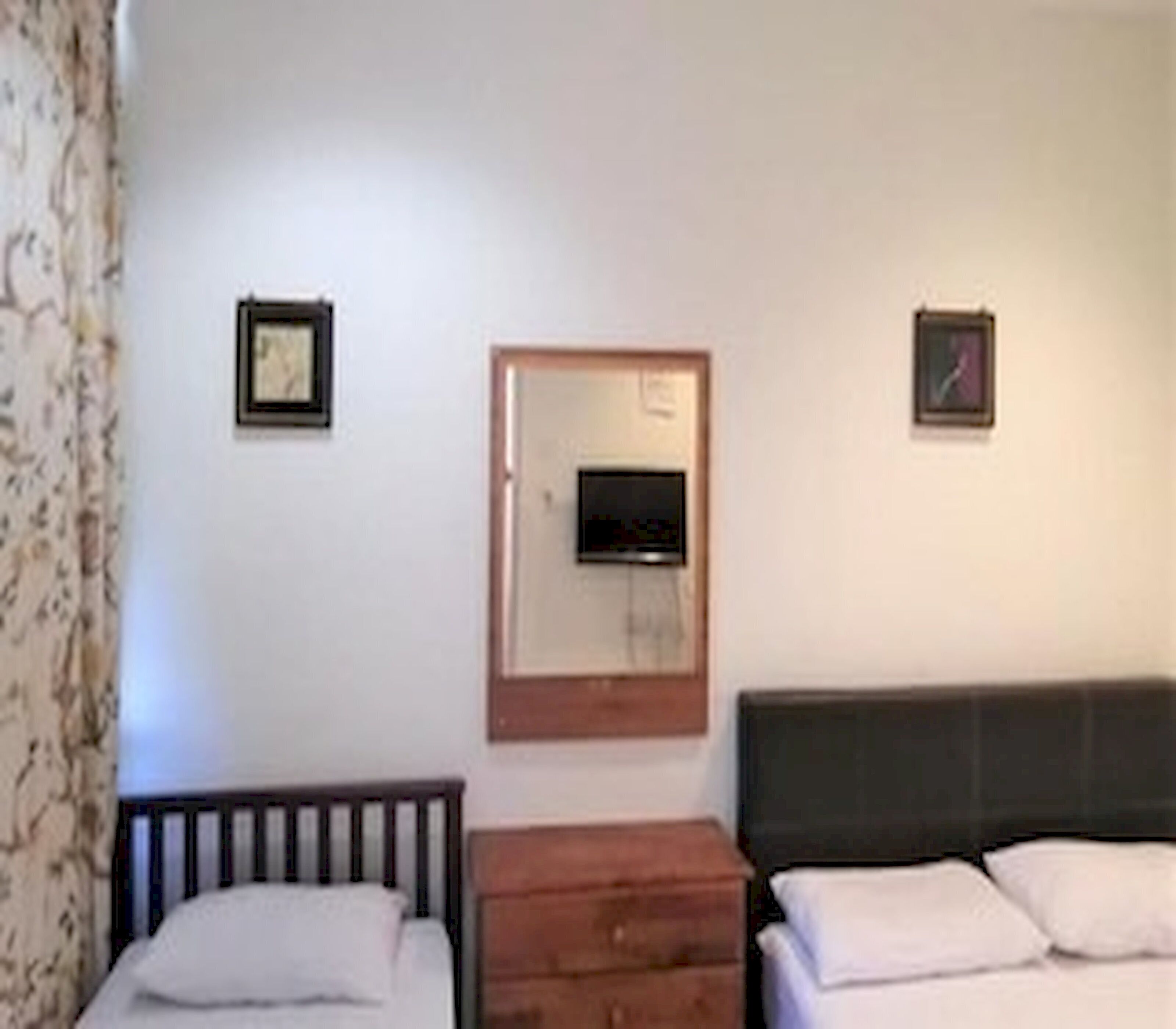 A room with two beds, a wooden dresser, a television mounted on the wall, and a framed picture.