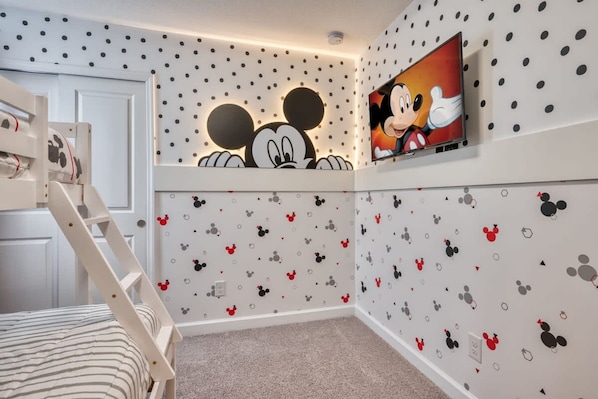 Une chambre d’enfant décorée avec des autocollants de Mickey Mouse, avec une télévision et un lit superposé.