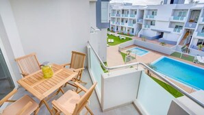 Ein Balkon mit Holztisch und -stühlen, der einen Pool und einen angelegten Garten blickt.