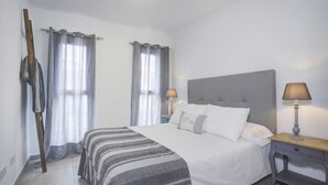 Ein Hotelzimmer mit einem Bett, zwei Nachttischen mit Lampen, einer Kopfteil und Vorhängen.