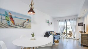Ein modernes Wohnzimmer mit einem weißen Esstisch, einem blauen Sofa und einem Gemälde, das eine Strandansicht zeigt.