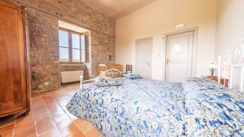 Ein Schlafzimmer mit einer Steinstur, einem großen Bett mit blumigem, blauem Überwurf, einem Holzschrank und einem Fenster mit Blick.