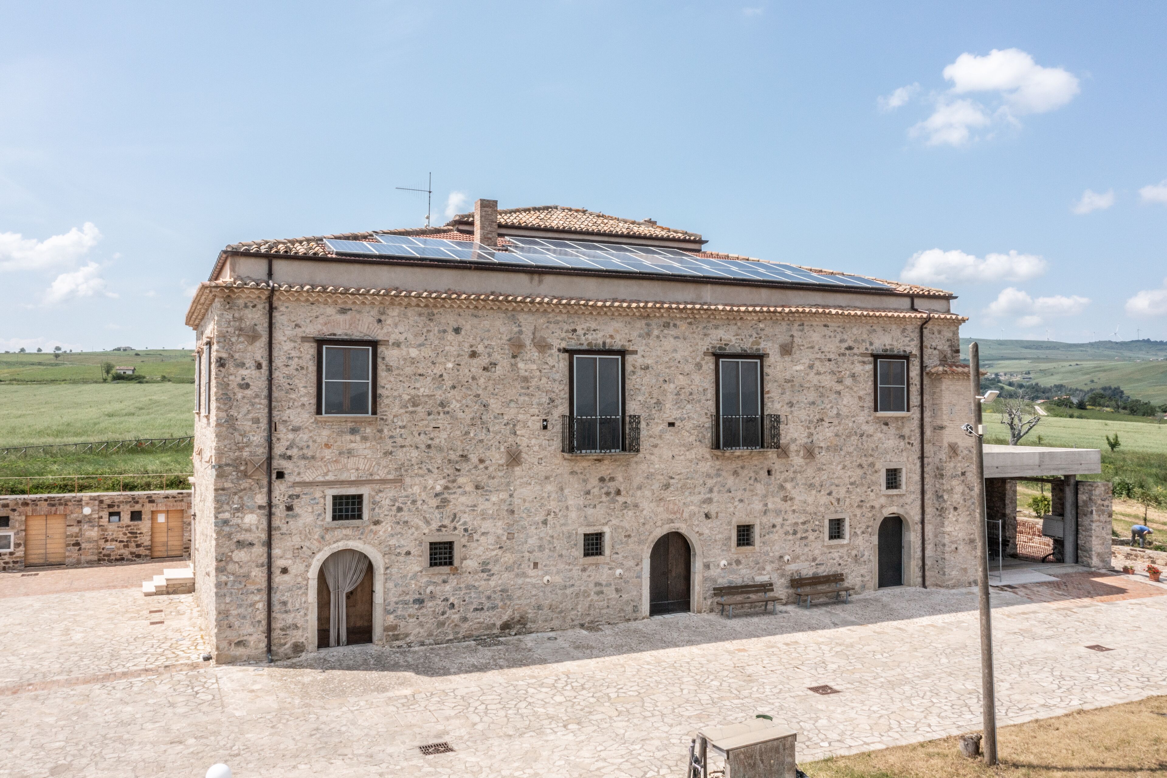 A stone building with a tiled roof, multiple windows, and a paved courtyard.