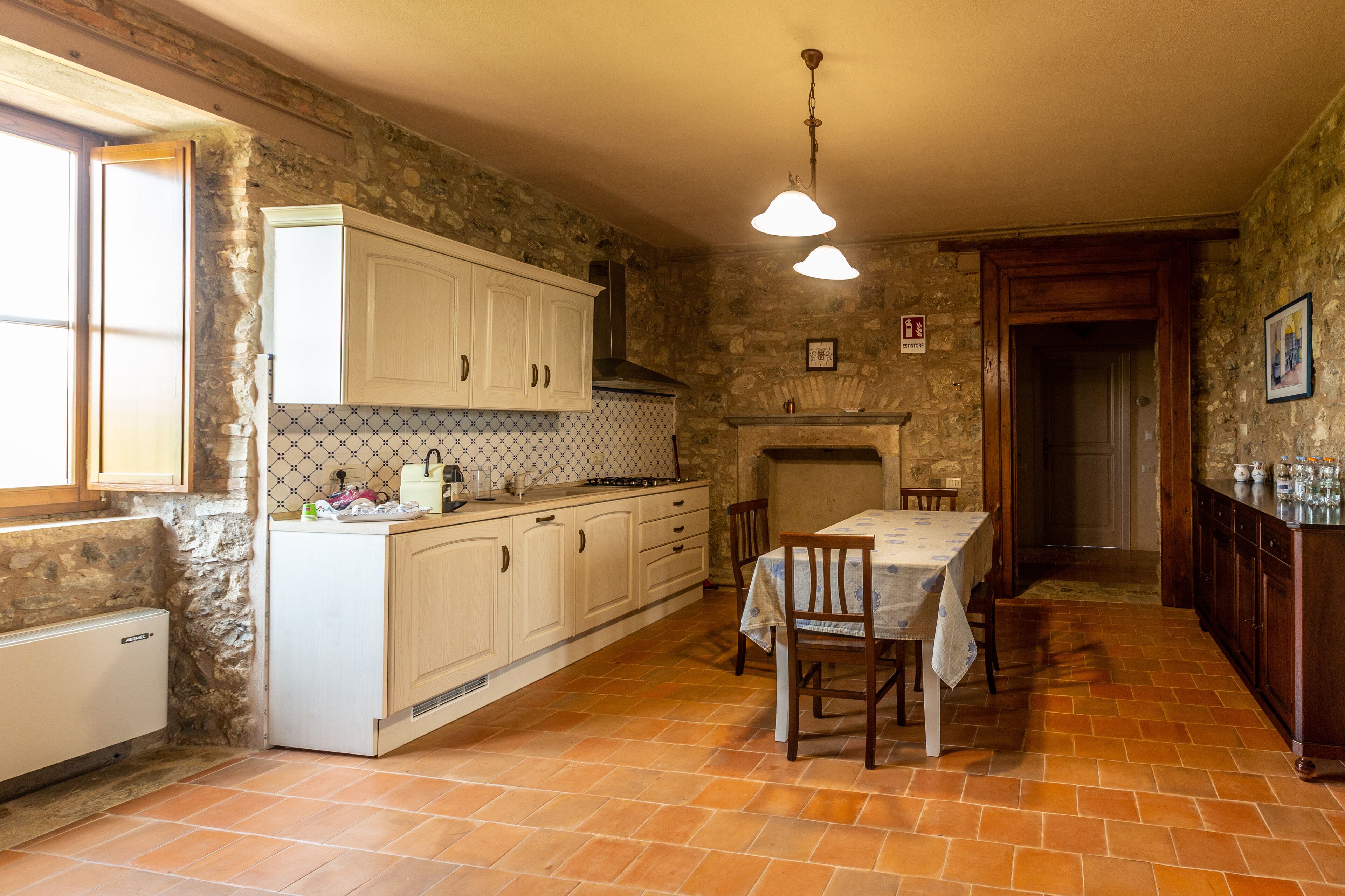 A rustic kitchen with stone walls, white cabinetry, and a tiled floor.
