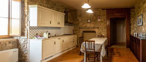 A rustic kitchen with stone walls, white cabinetry, and a tiled floor.