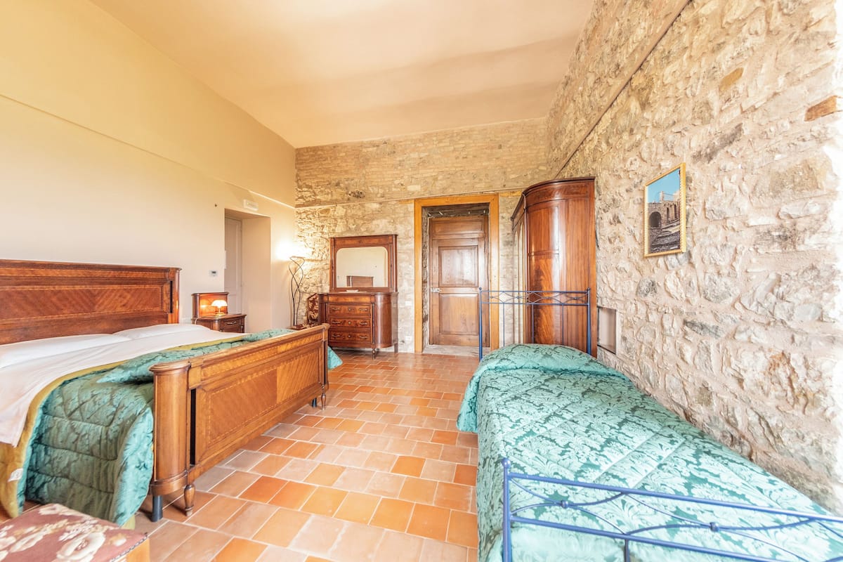 Un dormitorio con pared de piedra, una cama de madera, un aparador de madera y un espejo.
