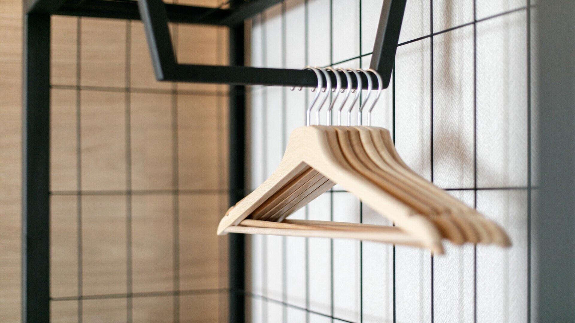 A wooden hanger with a triangular shape, hanging on a metal rack against a tiled wall.