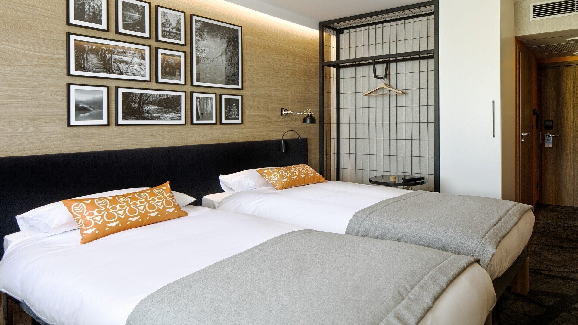 Een hotelkamer met twee bedden, een houten hoofdbord, een tv aan de muur en een kapstok.