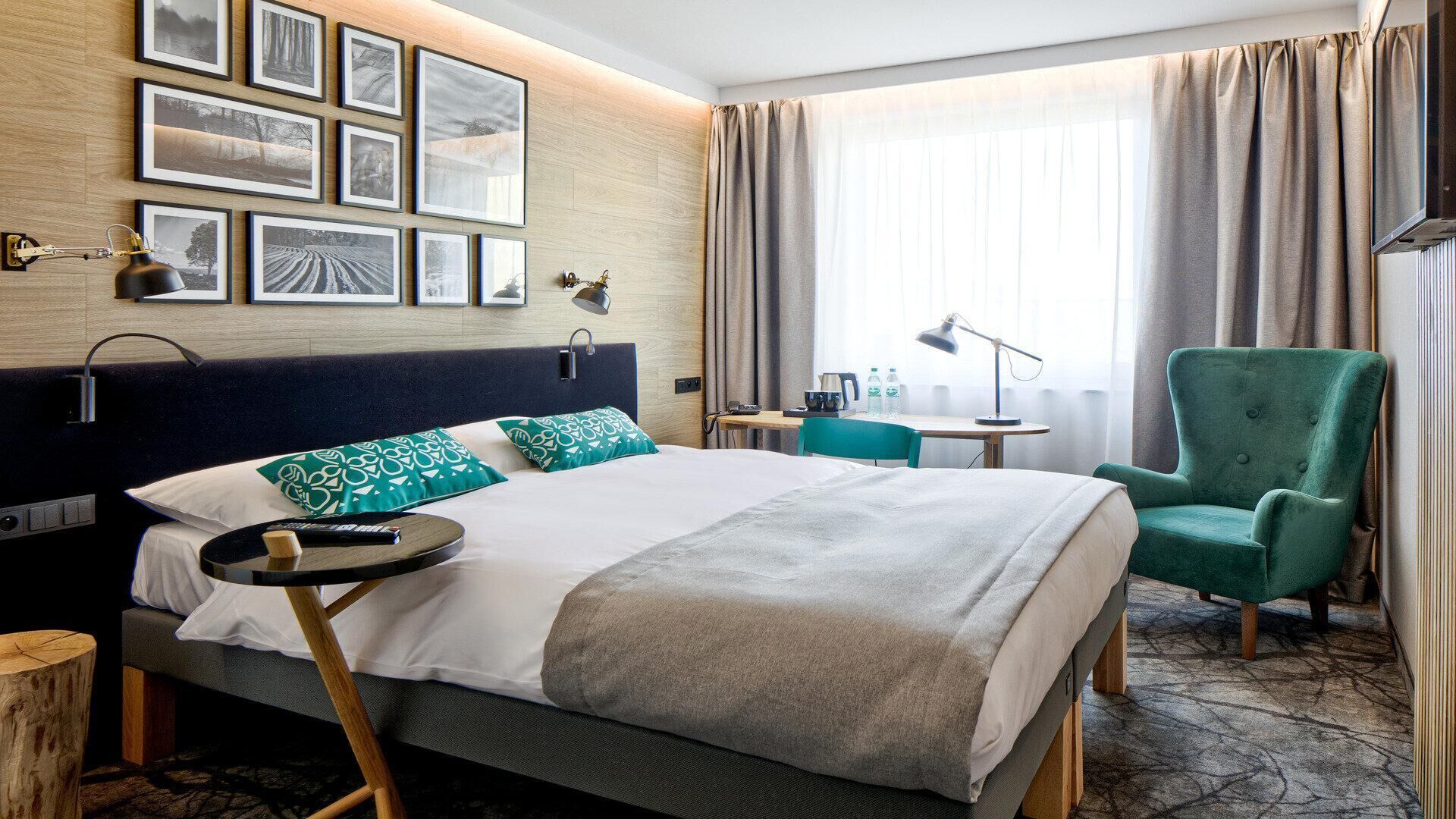 Een hotelkamer met een bed, een bureau, een stoel en een muur met ingelijste foto's.