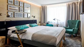 Een hotelkamer met een bed, een bureau, een stoel en een muur met ingelijste foto's.