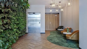 A hotel reception area with a wooden herringbone floor, a green carpet, a reception desk, two chairs, a wall of green plants, and a wooden door labeled "HOTEL & RESTAURACJA". - B&B HOTEL Tomaszów Lubelski (Tomaszow Lubelski)