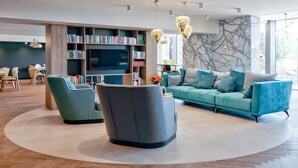 A modern living room with a sofa, armchairs, a coffee table, a TV, bookshelves, and a dining area. - B&B HOTEL Tomaszów Lubelski (Tomaszow Lubelski)