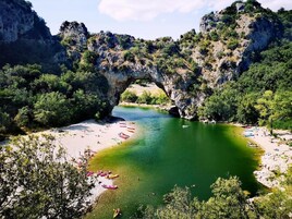 Un arco natural sobre un río, con una playa y barcos.