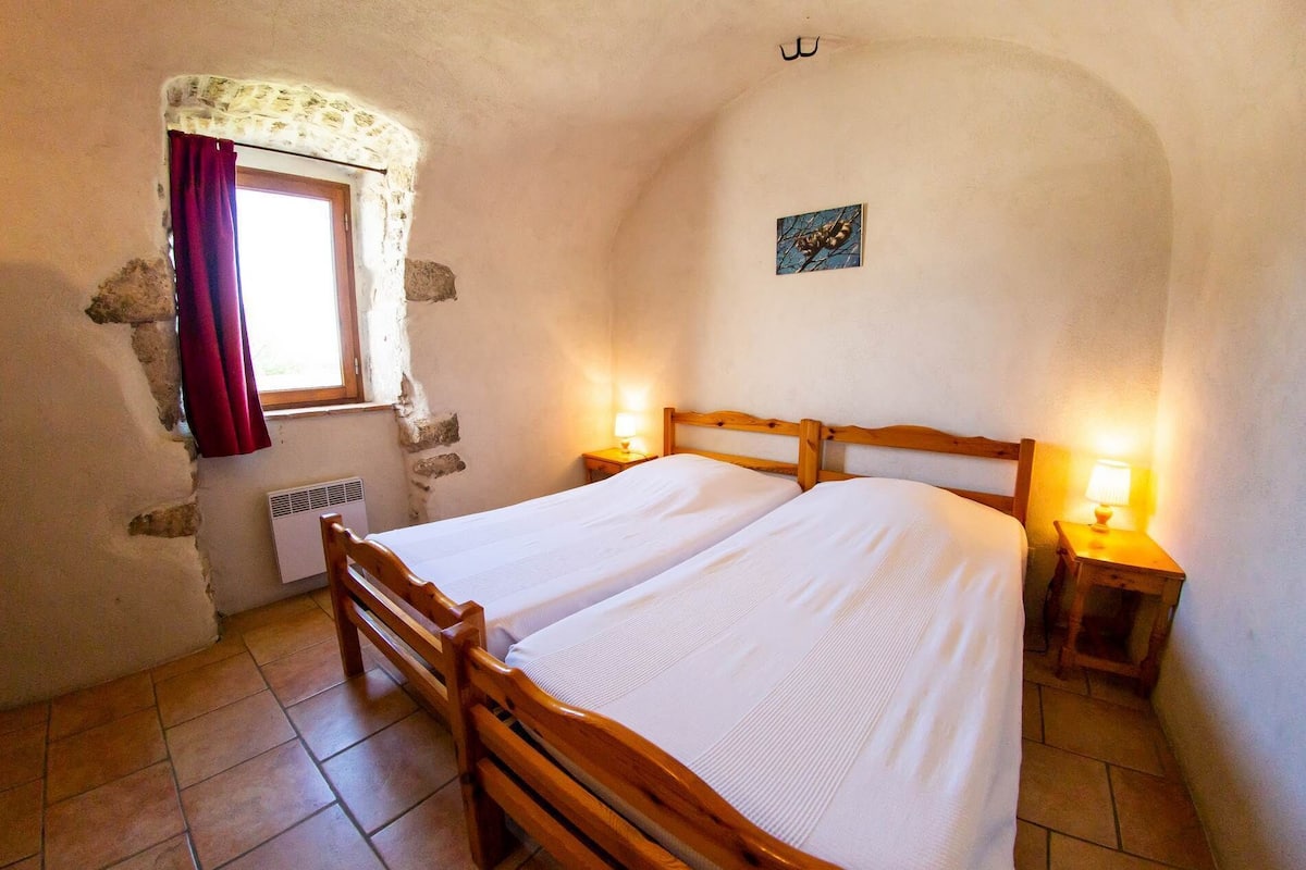 Een slaapkamer met een houten bed, twee nachtkastjes met lampen, een raam met gordijn, en een klein schilderij aan de muur.