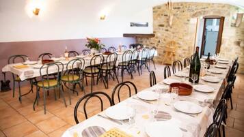 Zona pranzo con diversi tavoli apparecchiati per un pasto, pareti in pietra e arredamento rustico.