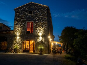 Un edificio de piedra con una entrada amplia y un ventanal, iluminado por luces exteriores.
