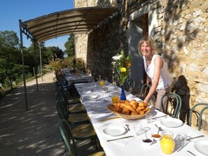 Un área de comedor al aire libre con una mesa larga dispuesta para una comida, rodeada de muros de piedra y follaje.