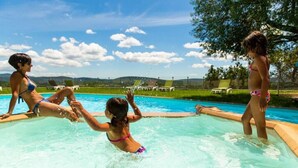 A swimming pool with three people in the water, surrounded by a grassy area and trees. - Domaine de l'Astic  (Vagnas)