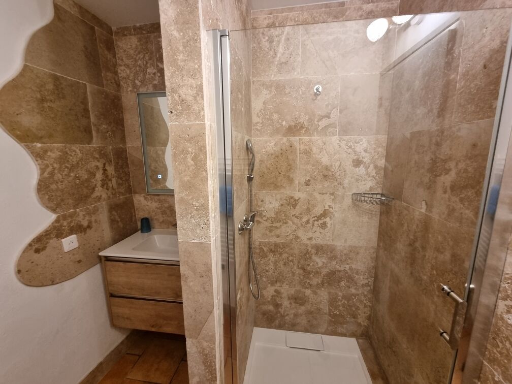 Een badkamer met een douche, wastafel en spiegel.