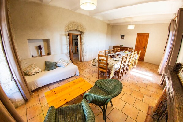 A cozy living room with a sofa, a dining table set for four, and a green chair. - Domaine de l'Astic (Vagnas)