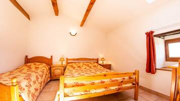 A bedroom with two wooden beds, a small table, a nightstand, a wall-mounted lamp, and a window with a curtain.