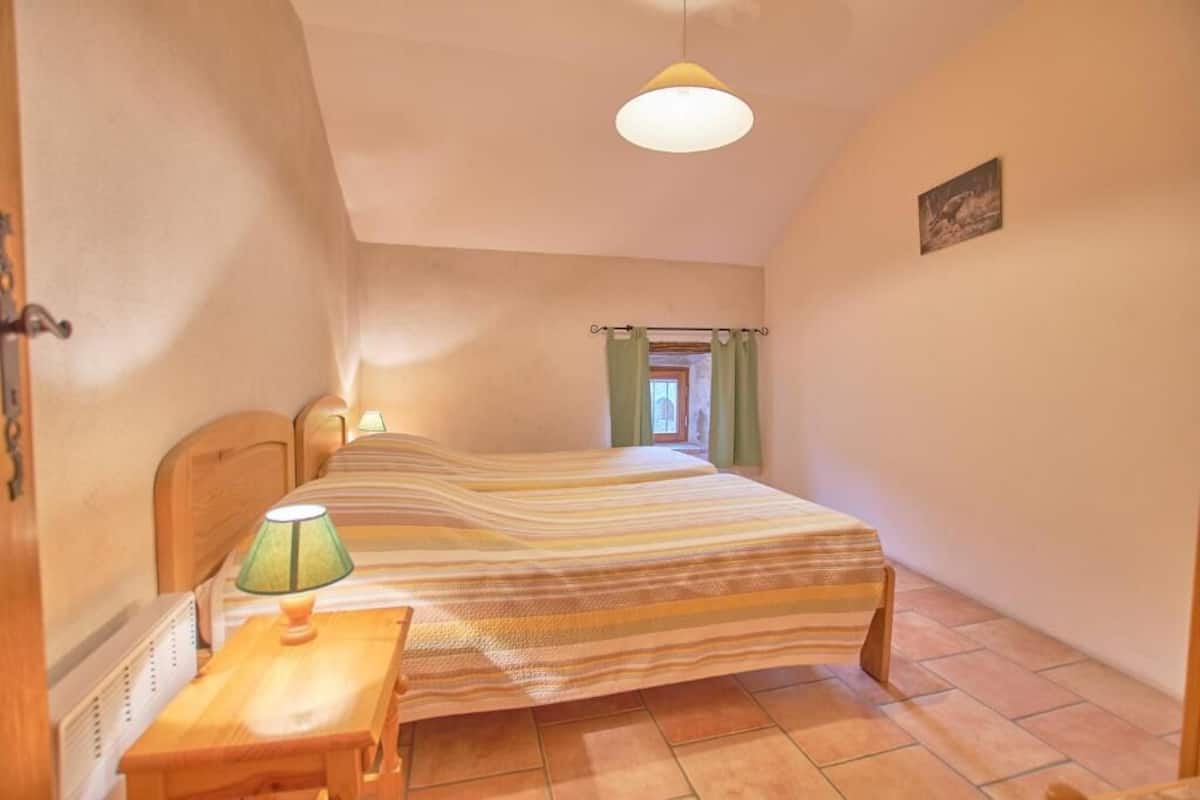 Een slaapkamer met een bed, nachtkastje, lamp, raam met gordijnen en een foto aan de muur.