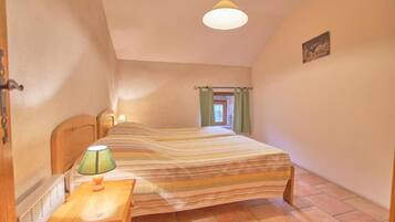 Une chambre à coucher avec un lit, une table de chevet, une lampe, une fenêtre avec des rideaux et un tableau au mur.