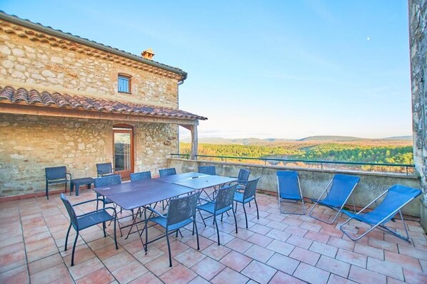 A stone building with a terrace, outdoor seating, and a view of the countryside. - Domaine de l'Astic (Vagnas)