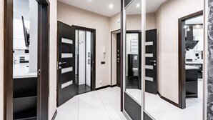 A modern hallway with a mirrored wall, a black-framed door, and a white tiled floor. - Apartment next to the shopping center (Minsk)