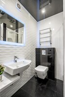 Ein modernes Badezimmer mit einem weißen Waschbecken, einem Spiegel, einer Toilette und einem Handtuchhalter.