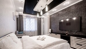 A modern hotel room with a large bed, a flat-screen TV, a brick-patterned accent wall, and a ceiling with recessed lighting. - Apartment next to the shopping center (Minsk)