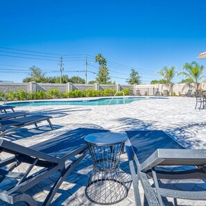 A pool area with lounge chairs and a table, surrounded by a stone wall and palm trees. - Super Spacious Villa With Private Pool and Themed Bedrooms (Kissimmee)
