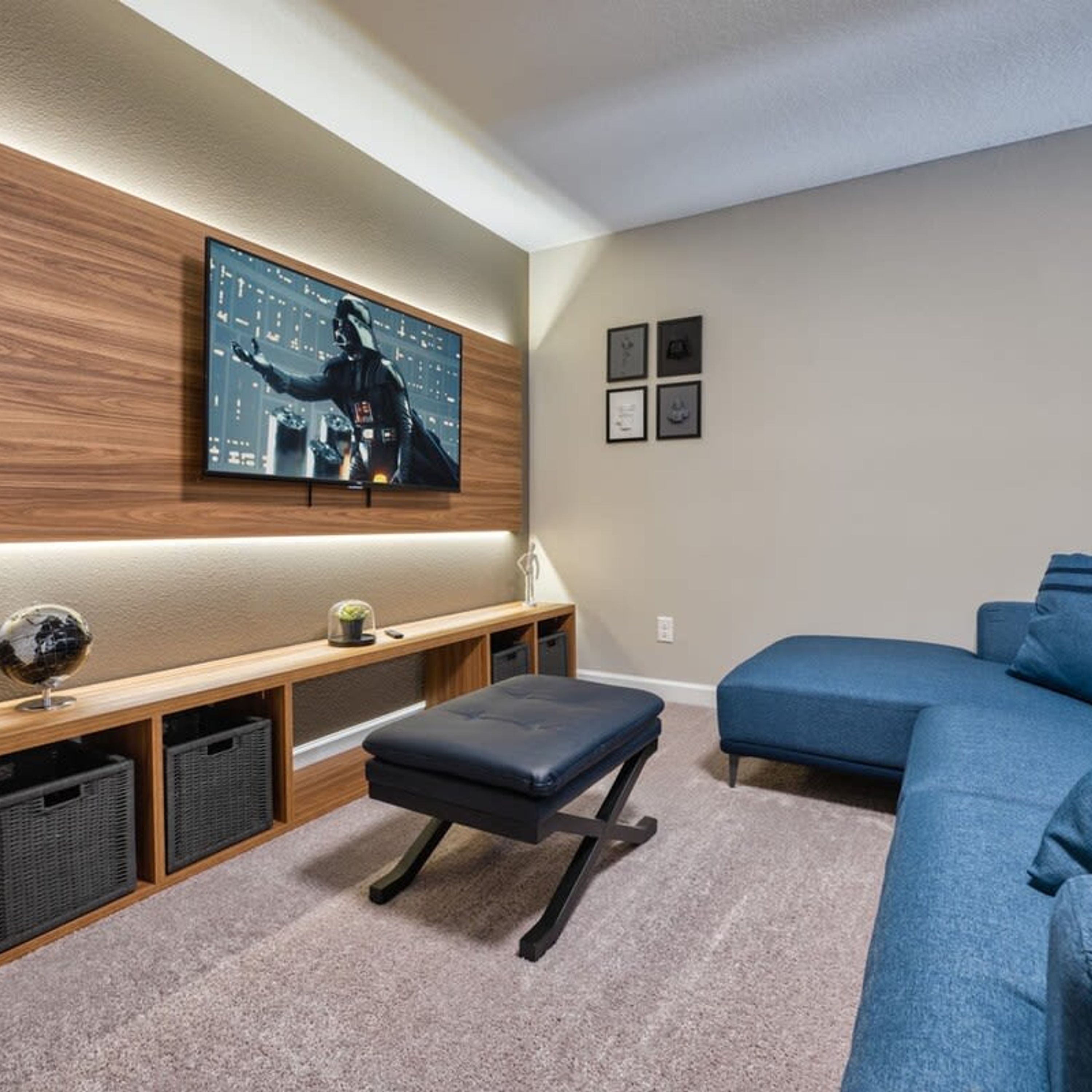 A modern living room with a large flat-screen TV mounted on a wooden wall, a bench, a blue sofa, and a small table with a globe and a plant.