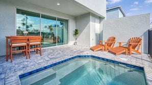 A swimming pool with wooden chairs and a table, surrounded by a paved patio. - Super Spacious Villa With Private Pool and Themed Bedrooms (Kissimmee)