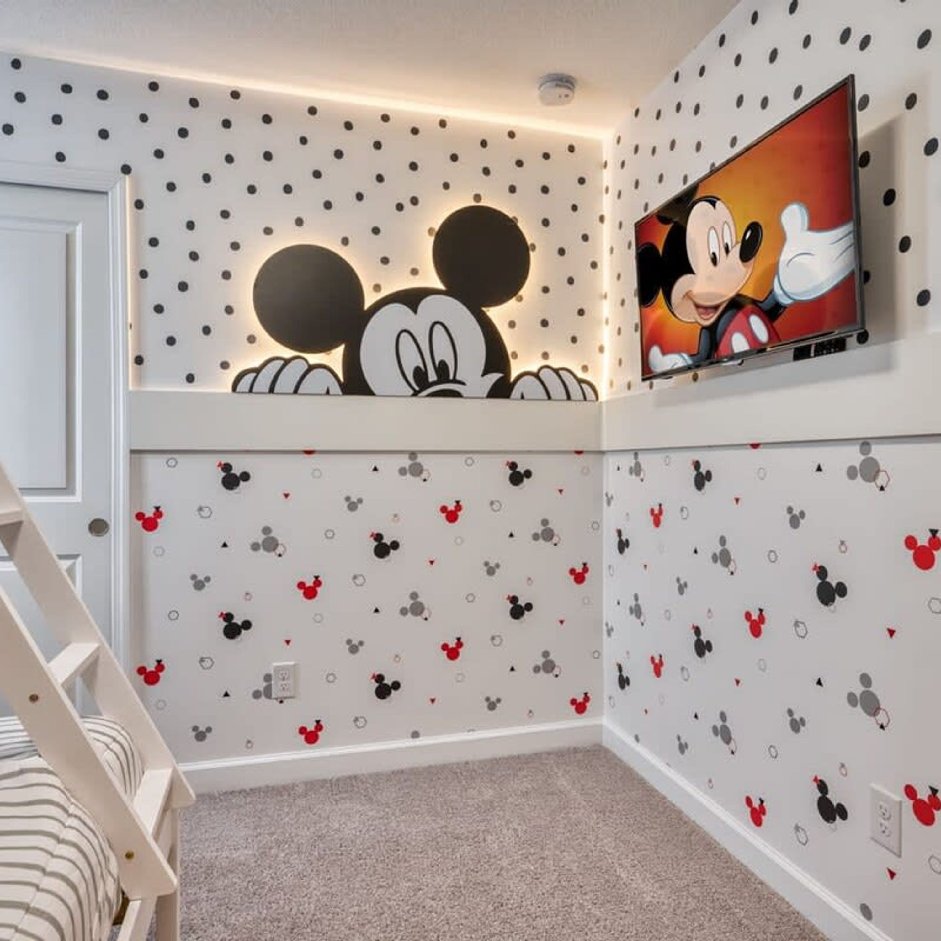 A room with Mickey Mouse wall decals, a television mounted above a shelf, and a white door.