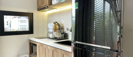 Cocina compacta con refrigerador negro, armarios de madera, salpicadero con motivo de espiga y ventana con vista a un edificio.