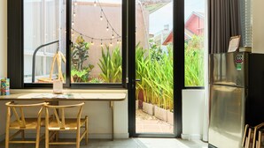 Une cuisine avec un coin repas, un réfrigérateur et une vue sur un jardin, visible à travers la porte ouverte.
